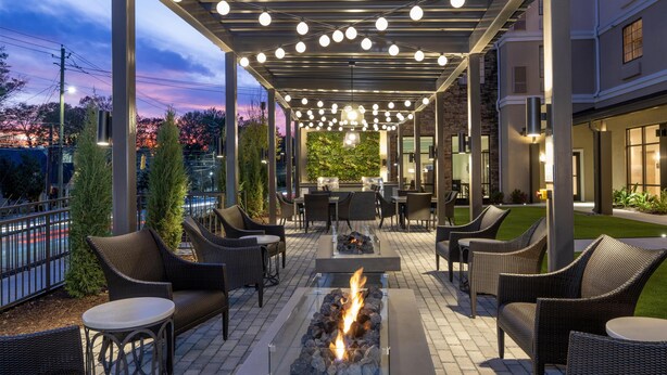 Un espace extérieur aménagé en patio, avec des meubles en osier, un foyer central et des guirlandes lumineuses.