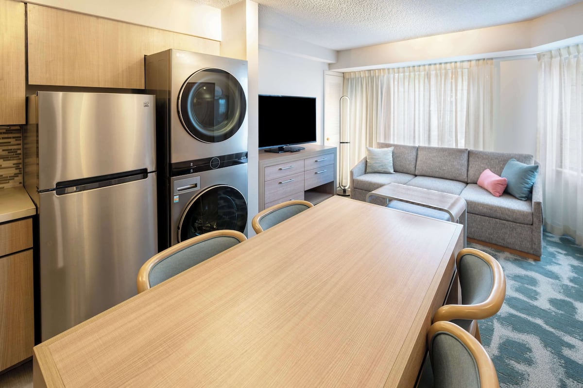 Kompakti hotellihuone, jossa on pieni keittiö, ruokapöytä, sohva ja televisio.