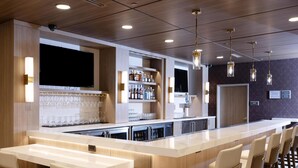 Un espace bar moderne avec un long comptoir, des tabourets de bar et un écran de télévision.