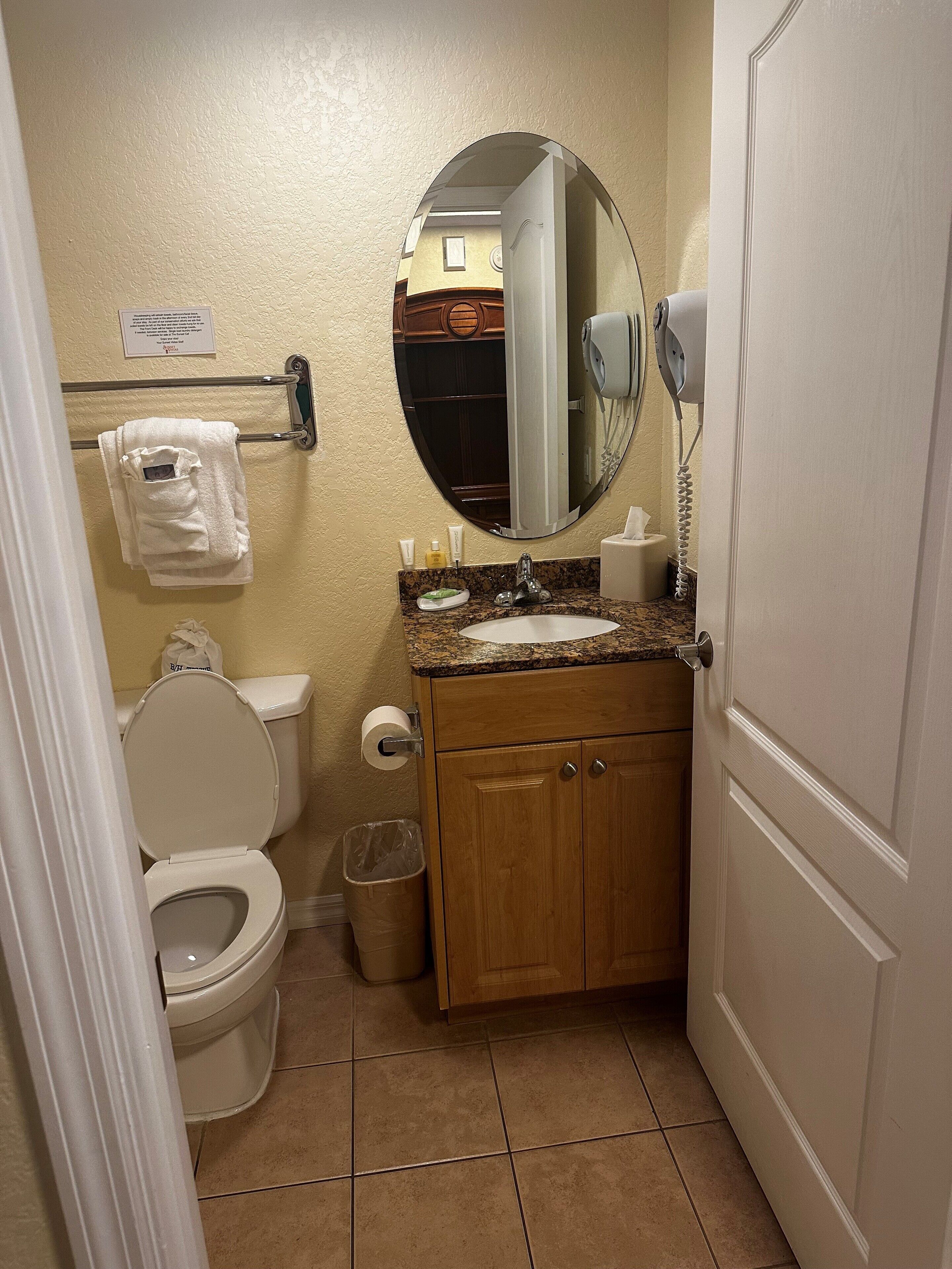 Un baño con inodoro, lavabo, espejo, toallero y cubo de basura.