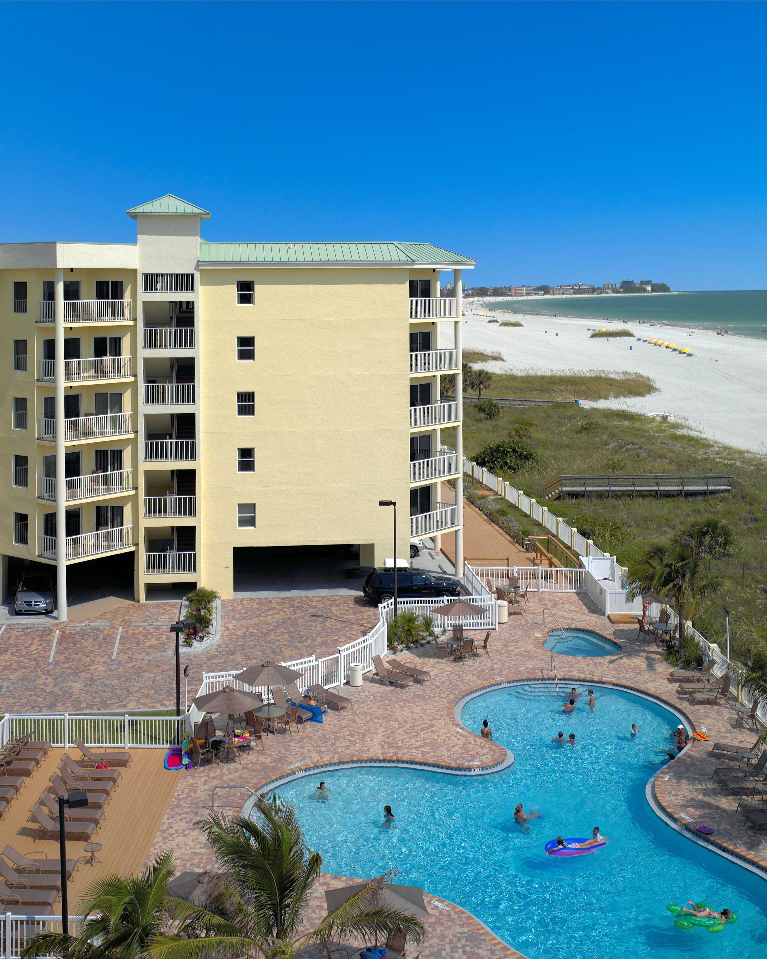 Um hotel com área de piscina, incluindo uma piscina grande e uma menor, rodeada por espreguiçadeiras e guarda-sóis.