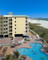Um hotel com área de piscina, incluindo uma piscina grande e uma menor, rodeada por espreguiçadeiras e guarda-sóis.