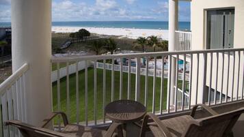 A balcony with wicker furniture, a view of a beach, and a pool area.