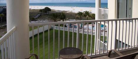 A balcony with wicker furniture, a view of a beach, and a pool area.