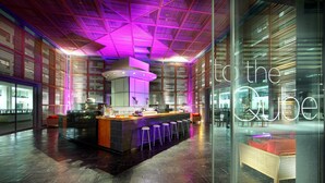 Een moderne bar met een centraal bar eiland, bar stoelen en een neonbord met de tekst 'to the cube'.