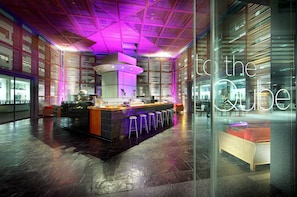 Uma área de bar moderna com uma ilha central, banquetas e um letreiro de neon com a inscrição "to the cube".