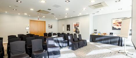 Un salón de conferencias con filas de sillas, un proyector y una mesa con refrigerios.