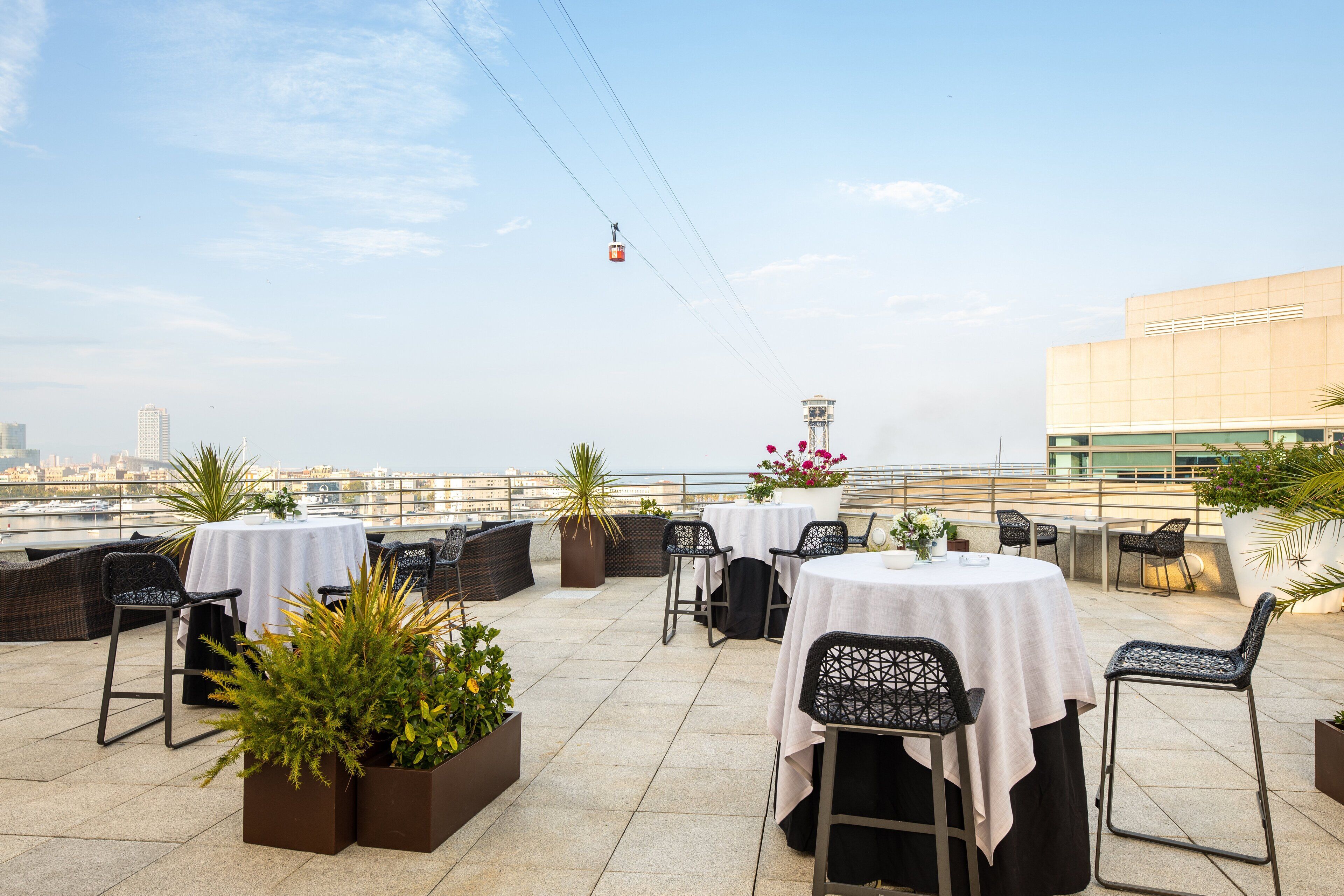 En tagterrasse med borde og stole, plantekasser og en kabelbane i baggrunden.