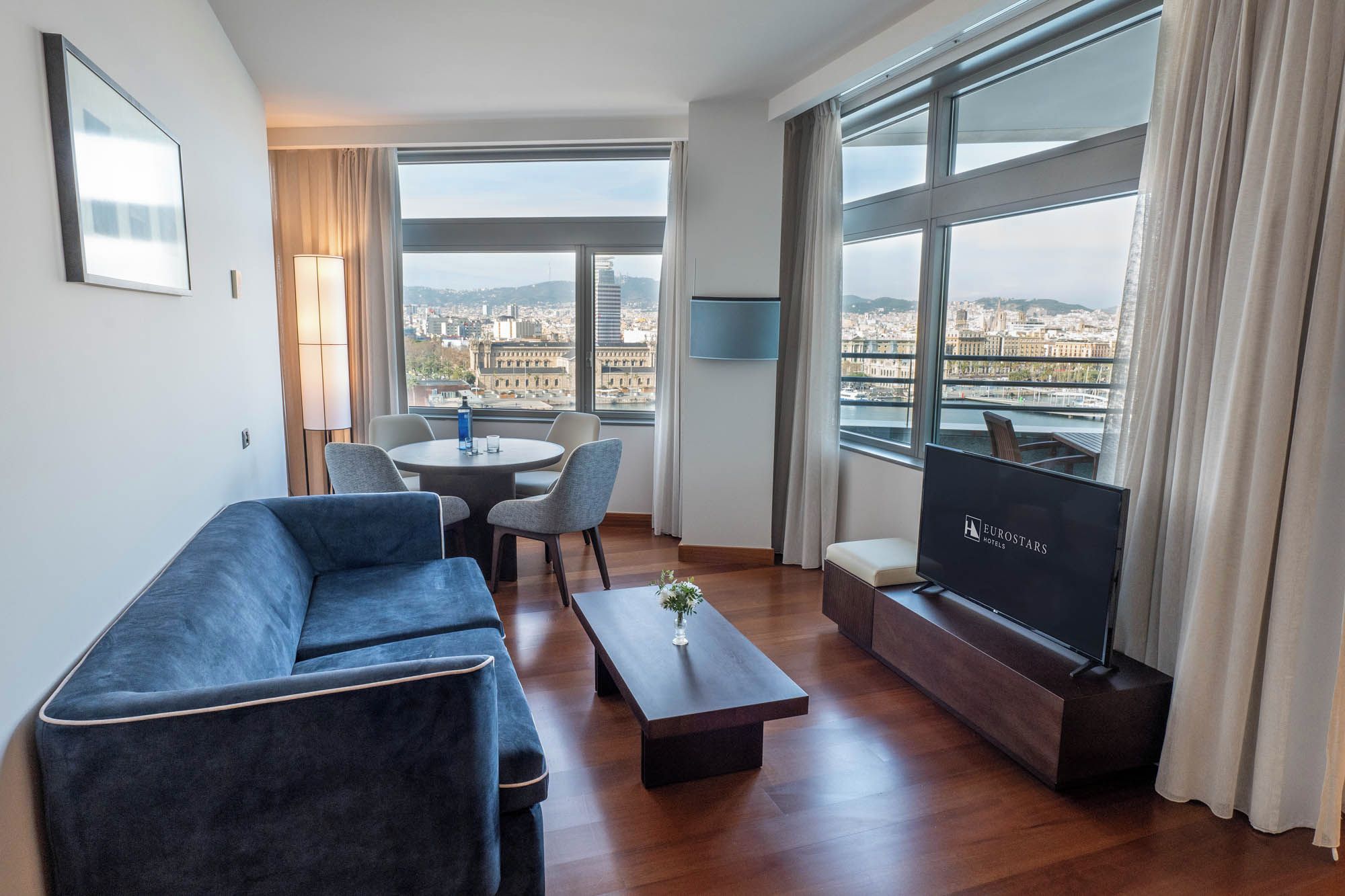 Une chambre d’hôtel moderne avec un canapé, une table basse, un téléviseur et une vue sur la ville.