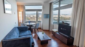 Une chambre d’hôtel moderne avec un canapé, une table basse, un téléviseur et une vue sur la ville.