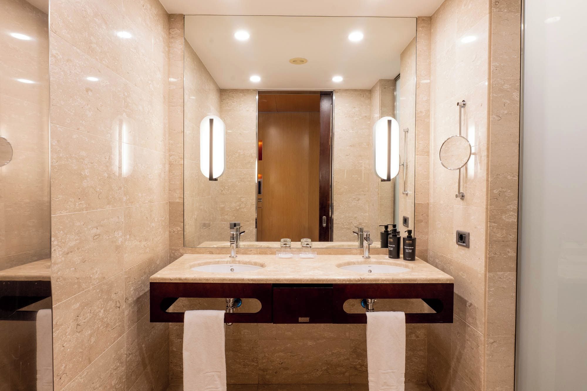 A modern bathroom with two sinks, a large mirror, and a towel rack.