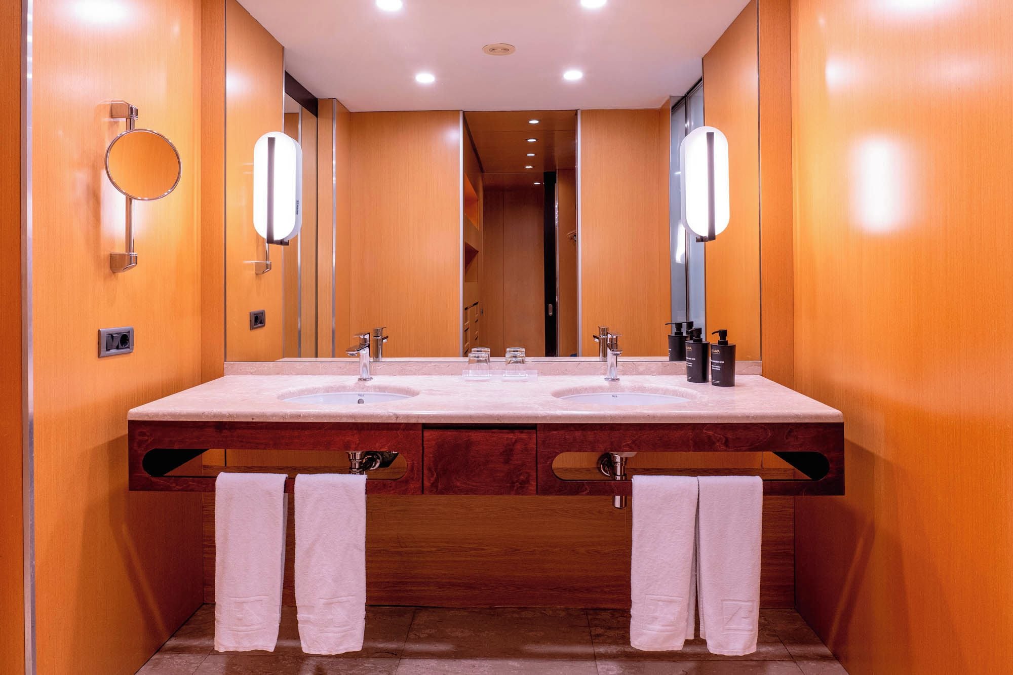 Un baño moderno con lavamanos doble, dos espejos y un mueble de tocador de madera.