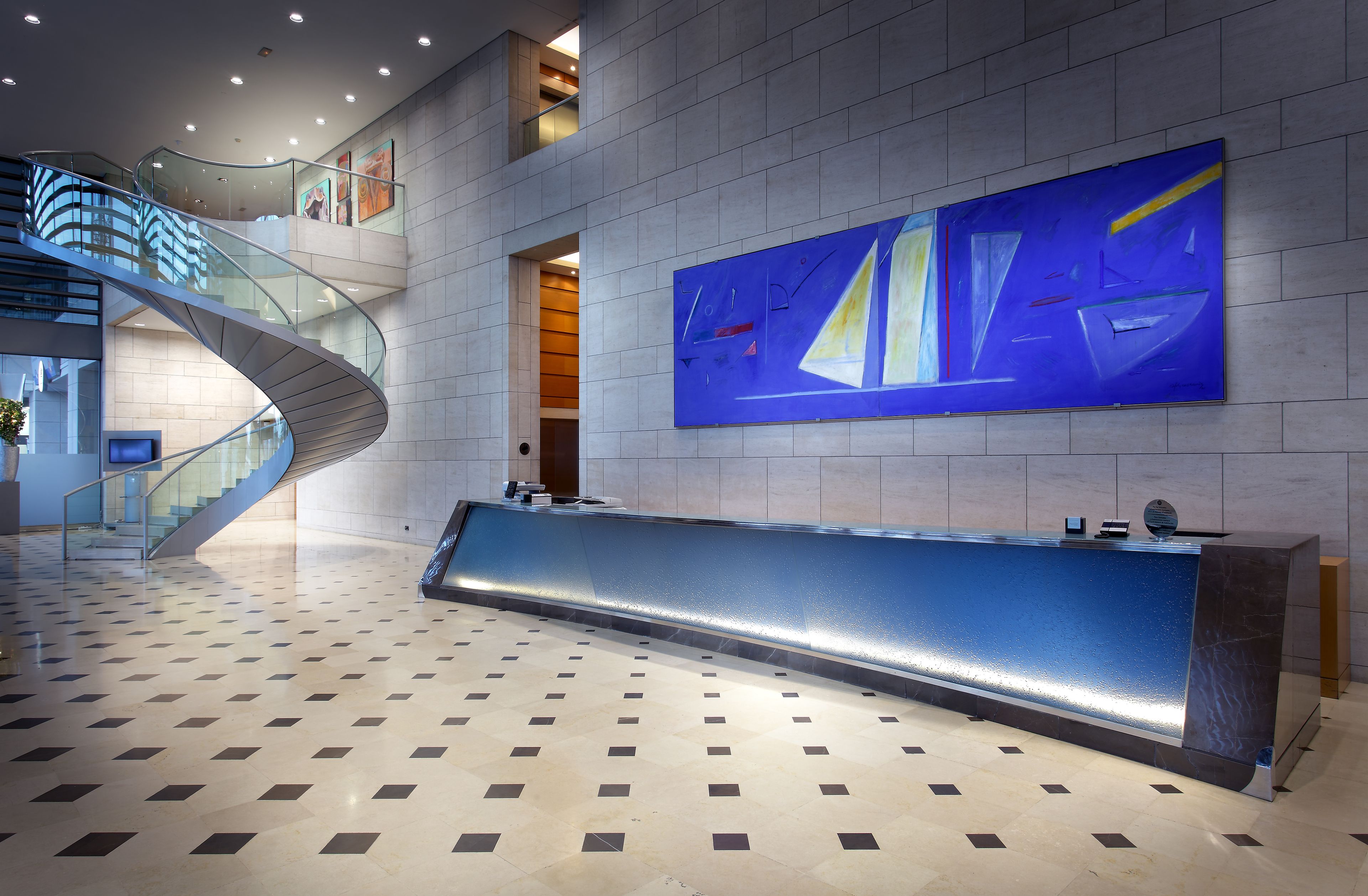 Een moderne lobby met een gebogen trap, een receptiebalie en een groot abstract schilderij aan de muur.