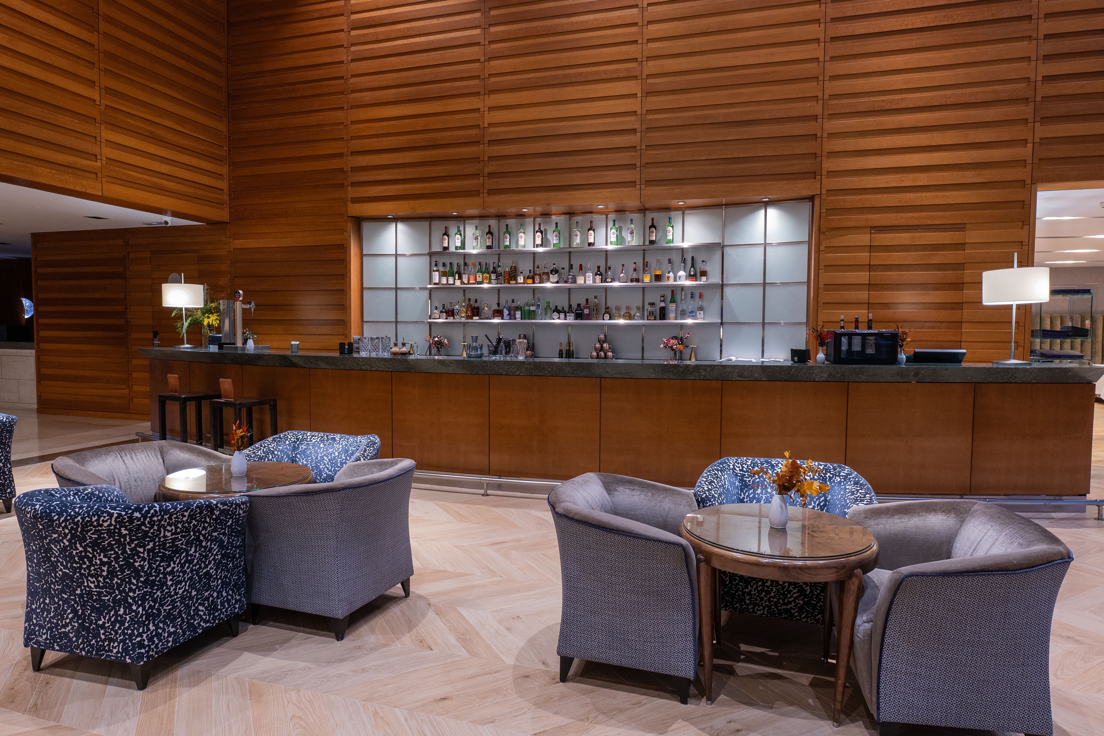 A bar area with a wooden backdrop, seating with patterned upholstery, and a variety of liquor bottles on shelves.