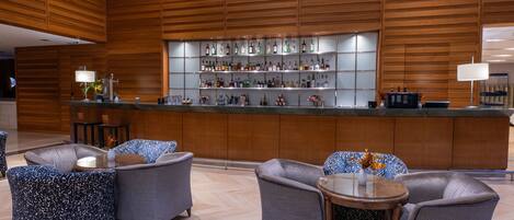 A bar area with a wooden backdrop, seating with patterned upholstery, and a variety of liquor bottles on shelves.
