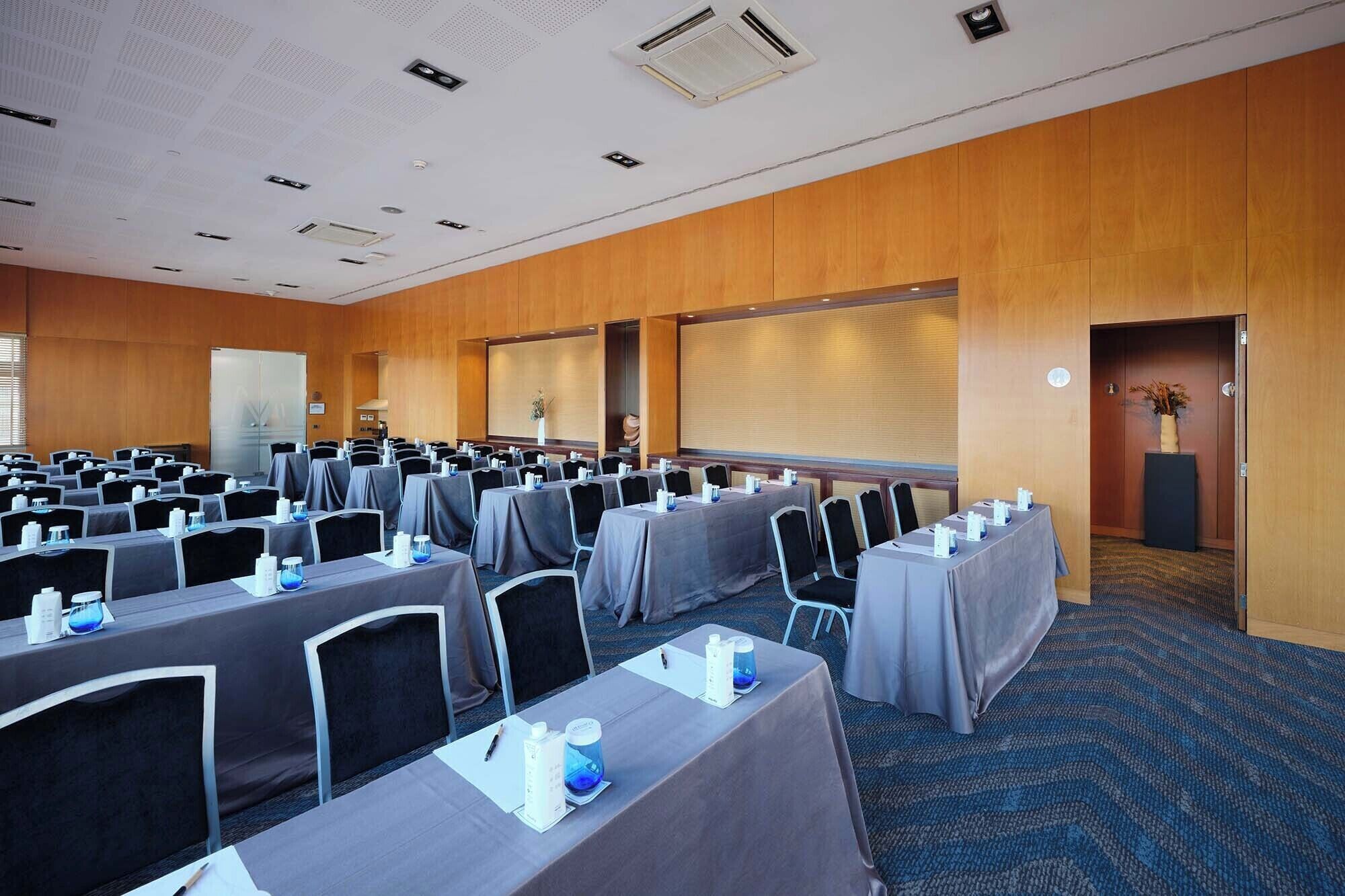 A conference room with rows of tables and chairs, a projector screen, and a whiteboard.