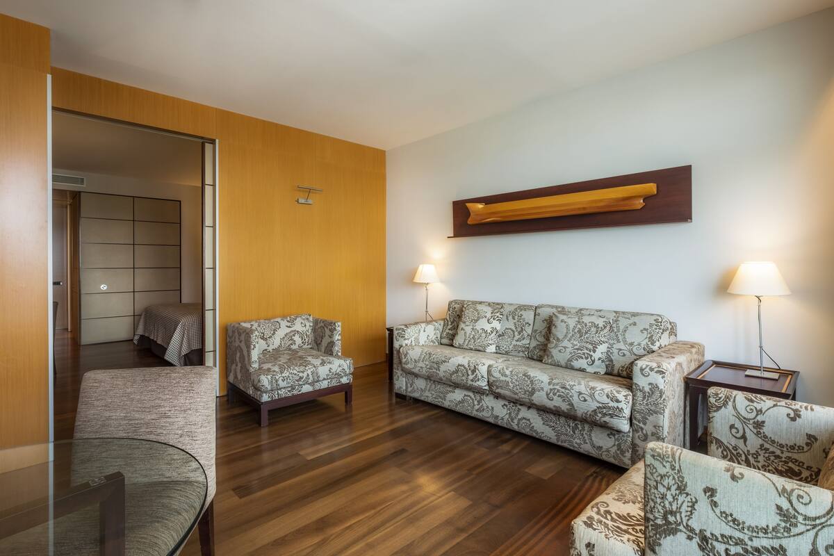 Een moderne woonkamer met een bank, twee fauteuils, een glazen salontafel en een houten vloer.