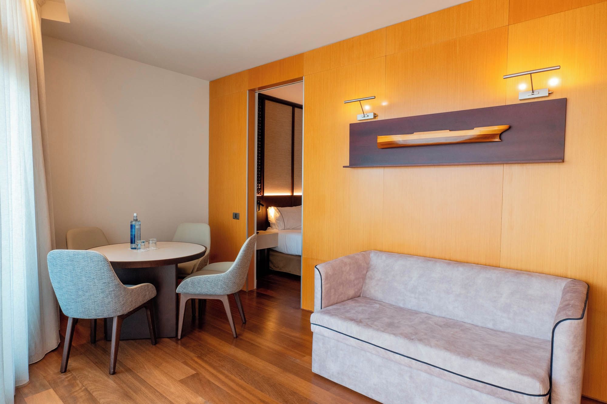 Habitación de hotel con pared de madera, un sofá, dos sillones, una mesita con una botella y una lámpara de noche.