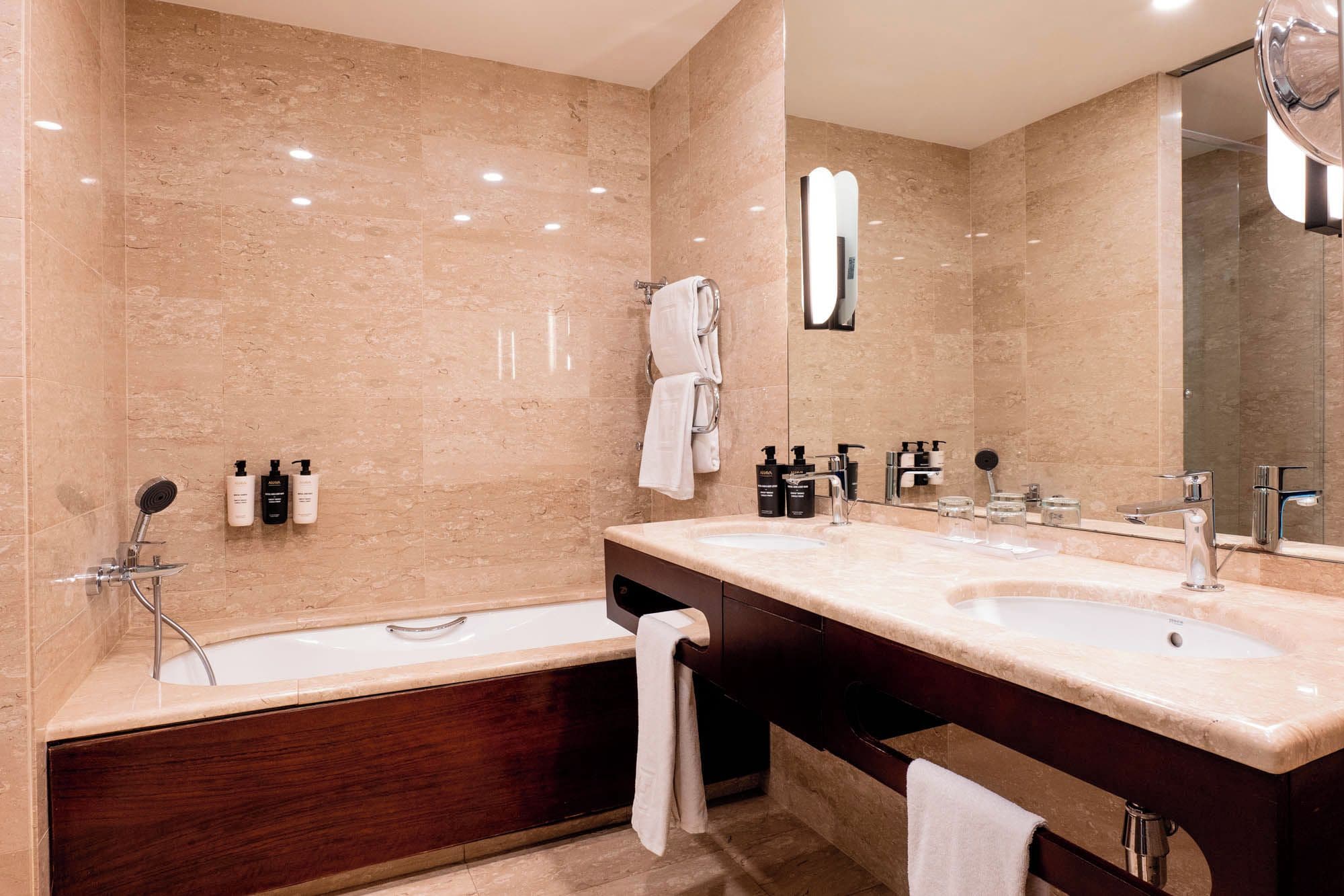 A modern bathroom with two sinks, a bathtub, and a large mirror.
