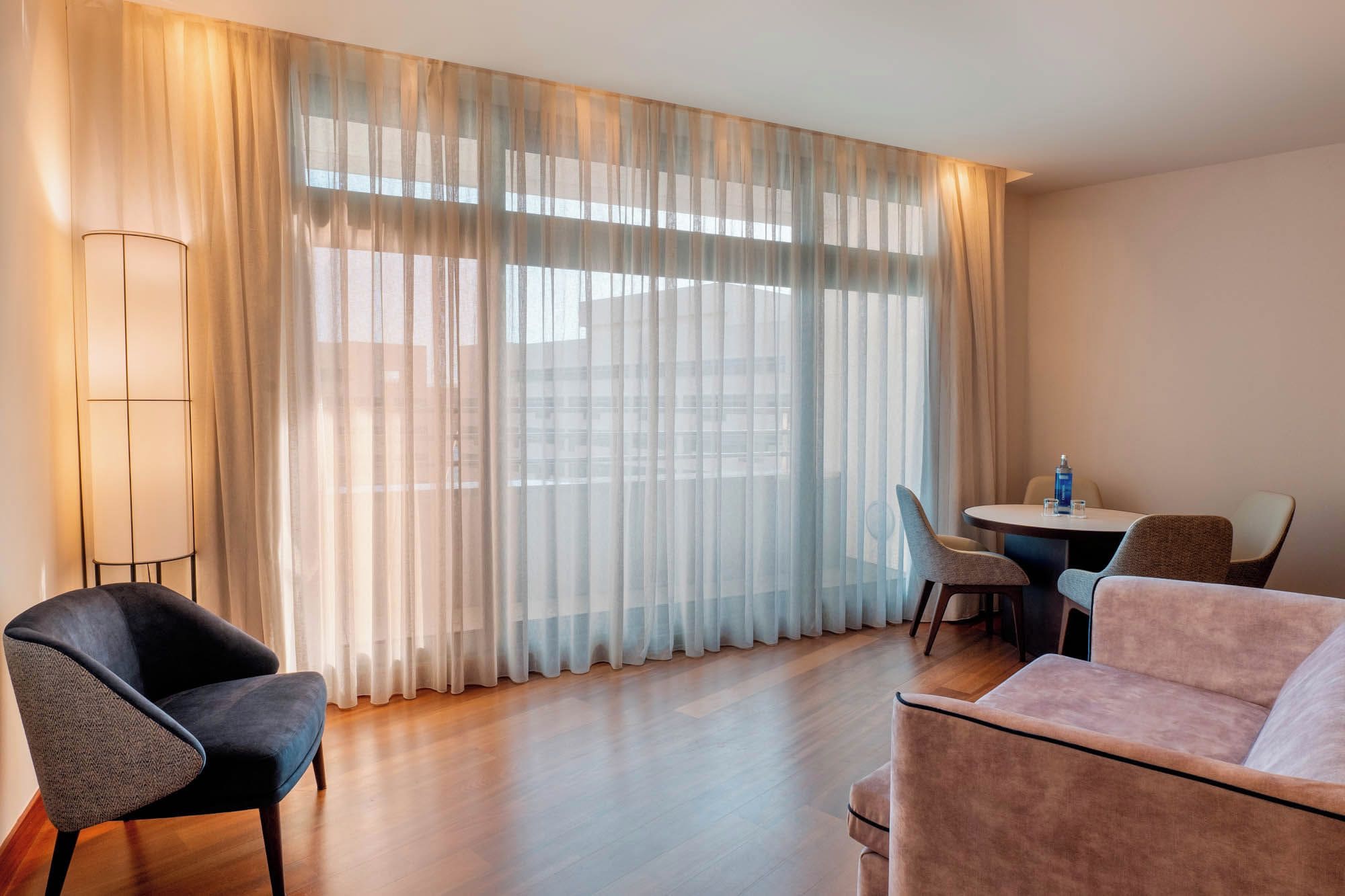 A hotel room with a large window, a dining table with chairs, and two sofas.