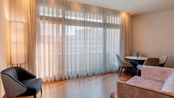 A hotel room with a large window, a dining table with chairs, and two sofas.