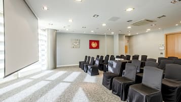 Une salle de conférence avec des rangées de chaises, un projecteur et un tableau blanc.