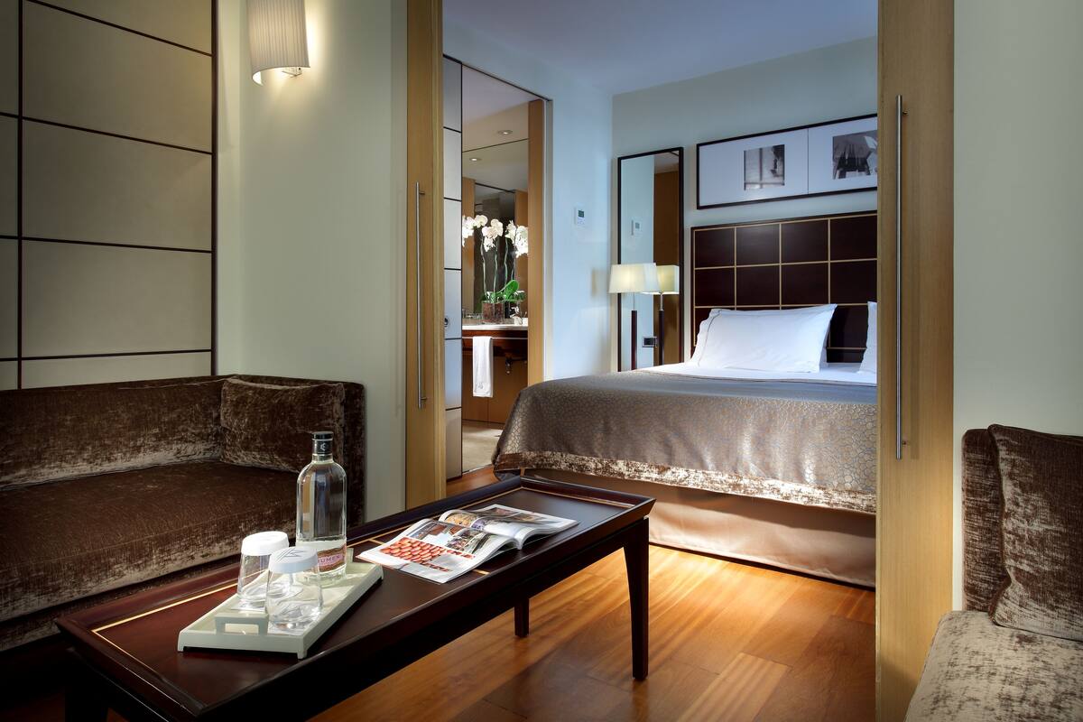 Een hotelkamer met een bed, een bank, een salontafel en een nachtkastje met een lamp.