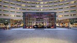 Een modern hotel met een gebogen gevel, meerdere balkons en een ruim buitenterrein met zitplaatsen.