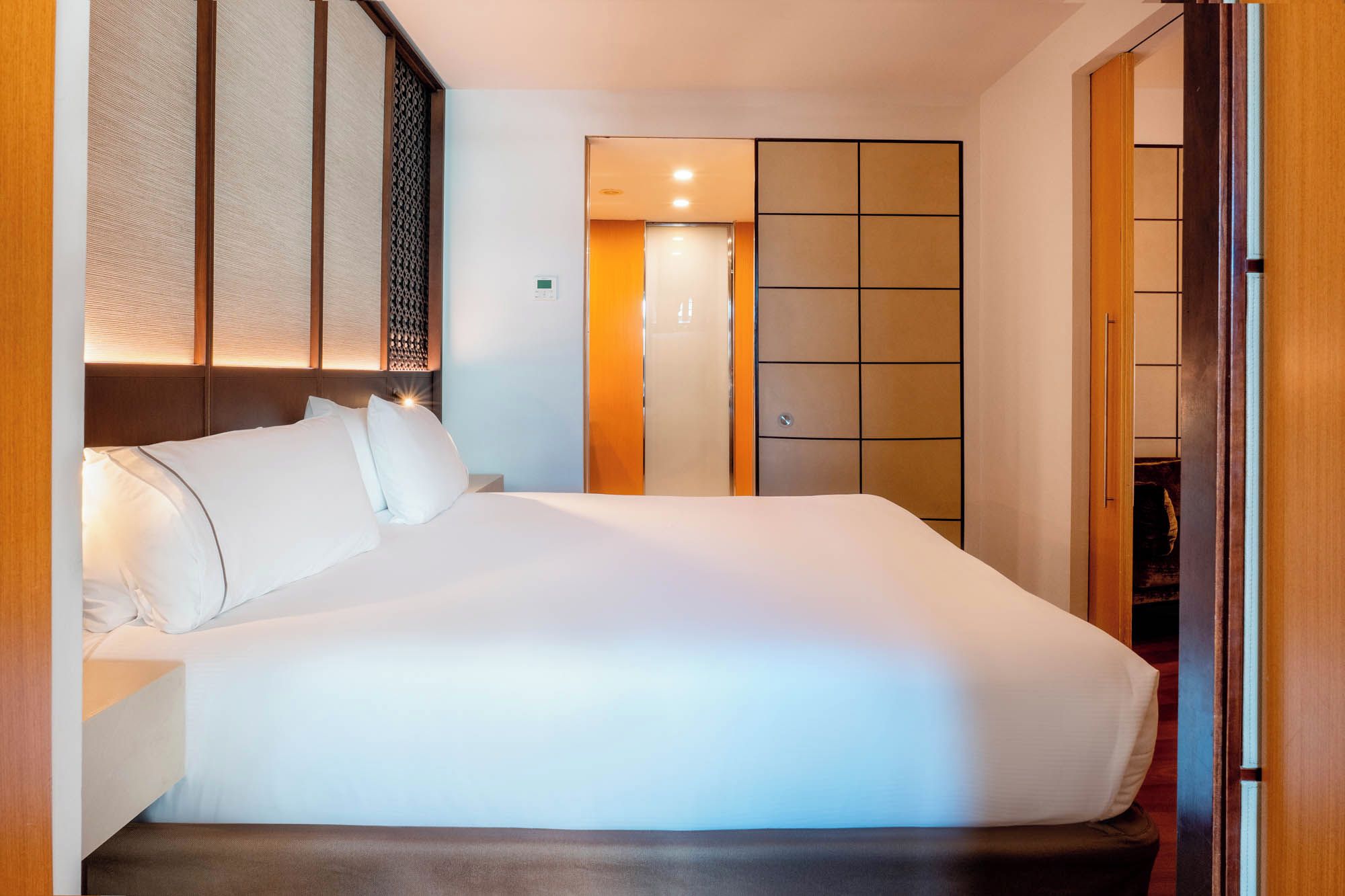 A hotel room with a large bed, a wardrobe, and a control panel on the wall.