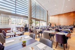 Un vaste espace dédié à la salle à manger, avec de nombreuses tables et chaises, de grandes fenêtres et un aménagement intérieur moderne.