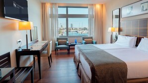 Habitación de hotel con una cama grande, un escritorio, dos sillas, un televisor y vistas al puerto deportivo.