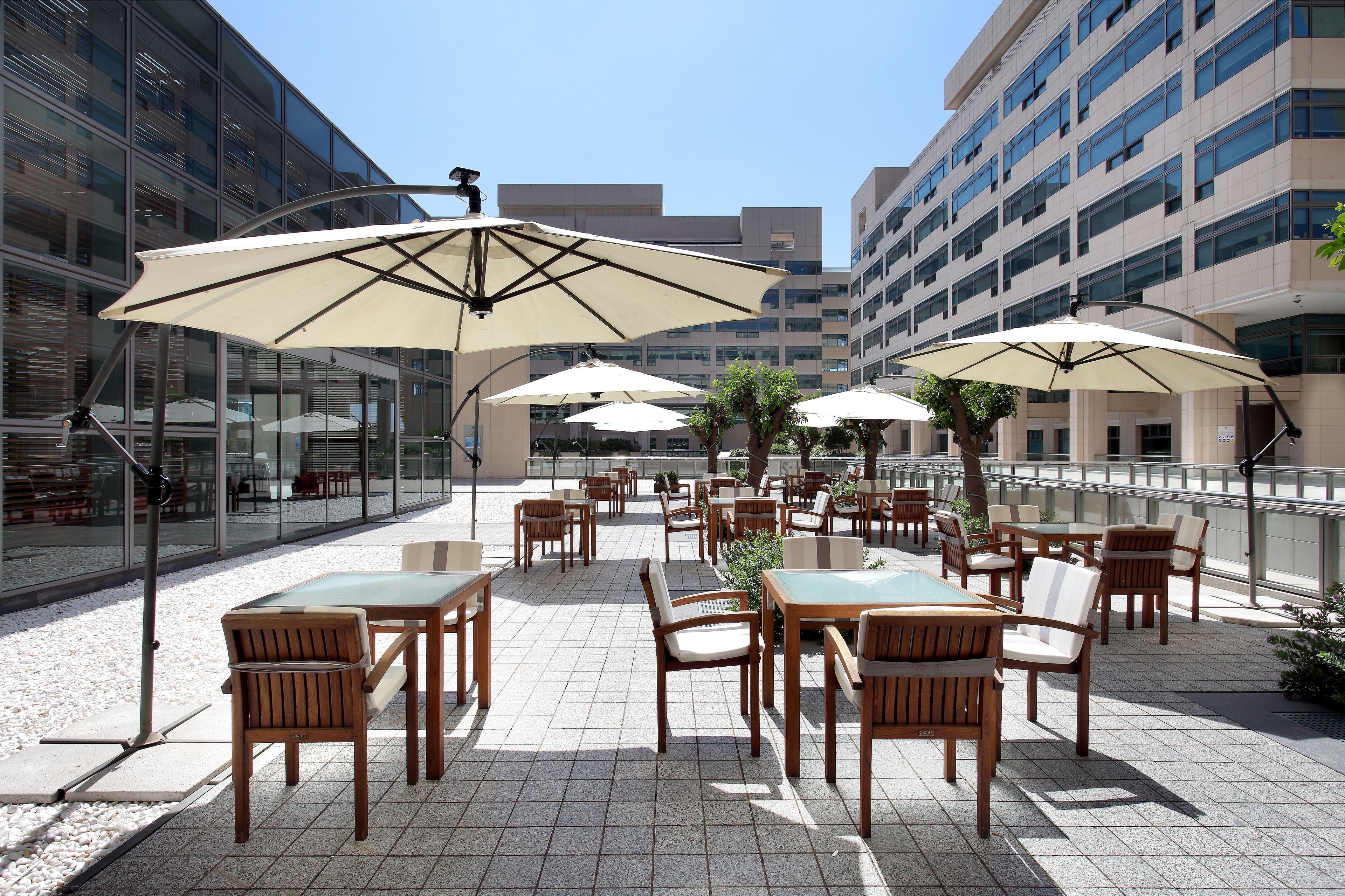 An outdoor patio with tables and chairs, large umbrellas, and a glass building in the background.