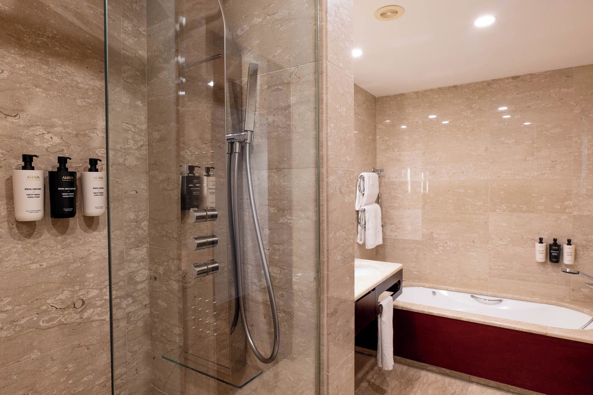 A modern bathroom with a glass-enclosed shower, a red bathtub, and toiletries on the wall.