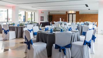 Un salón de banquetes con mesas redondas, sillas blancas con cintas azules y un suelo pulido.