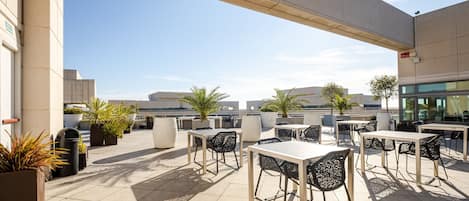 An outdoor patio area with tables and chairs, potted plants, and a clear sky.