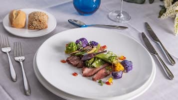 A white plate with a meal consisting of steak, vegetables, and a sauce.