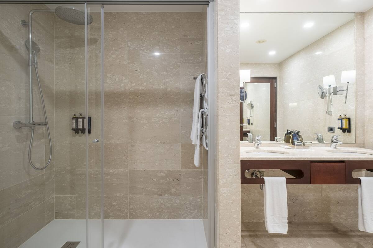 Een moderne badkamer met een douchecabine van glas, een wastafel met twee wasbakken en een grote spiegel.
