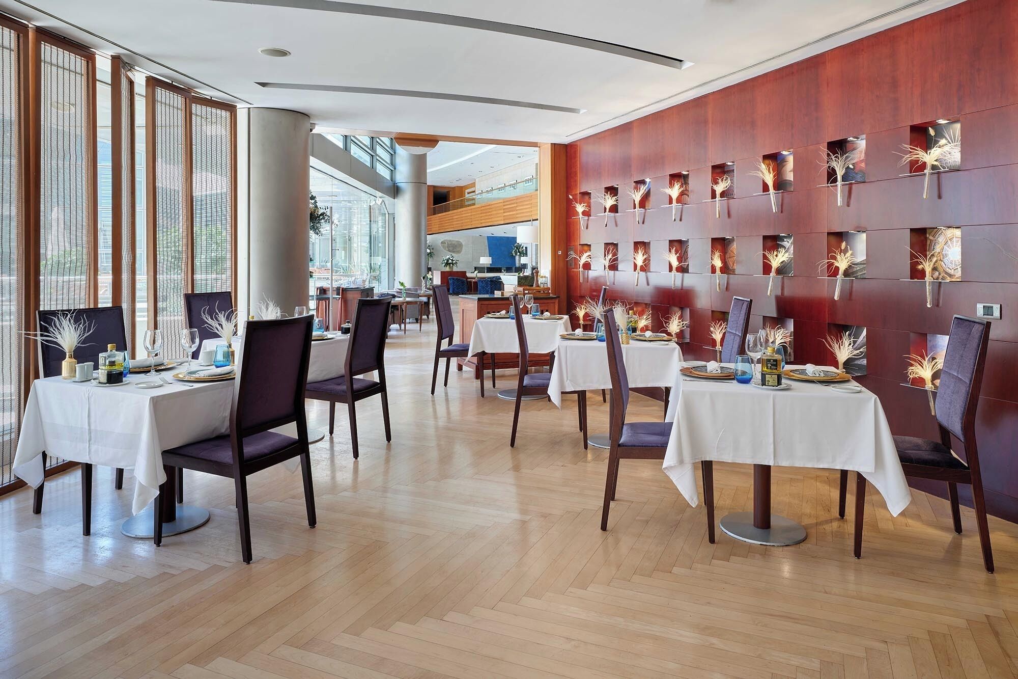 En restaurant med flere borde til spisning, med et moderne interiør, trægulve og en kombination af naturligt og kunstigt lys.