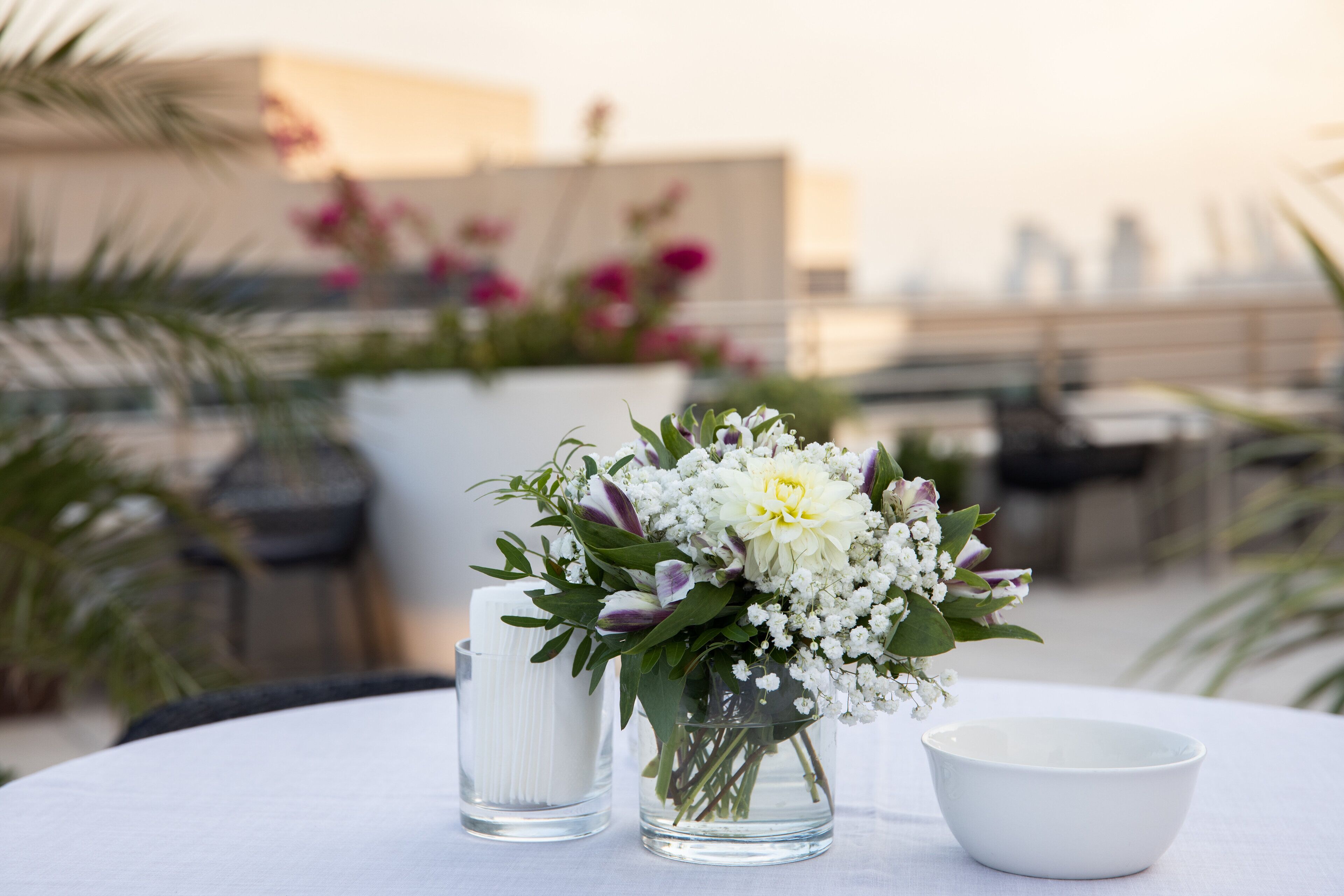 Uma mesa com um vaso branco com flores, uma vela branca e uma tigela branca.