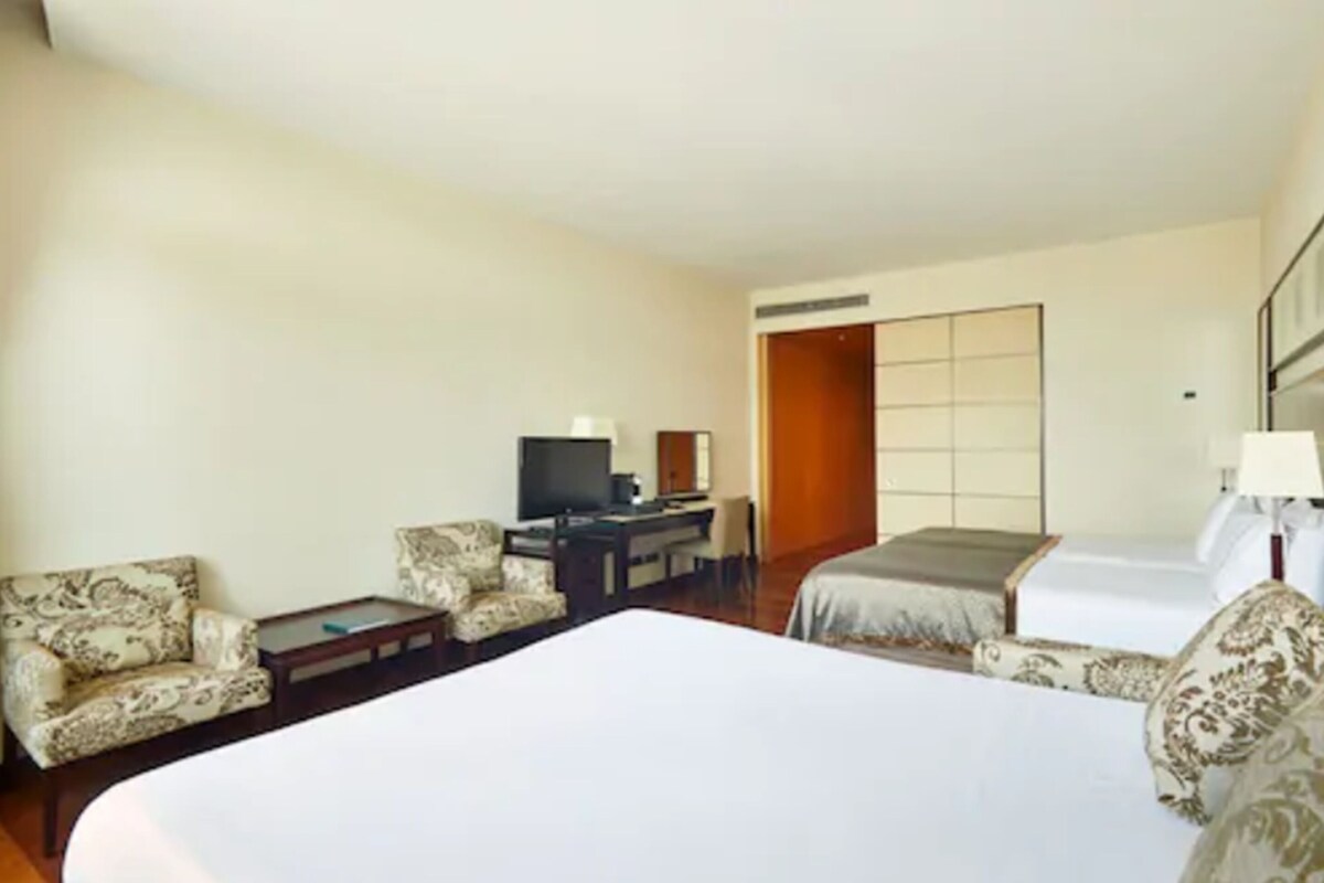 Quarto de hotel com uma cama grande, duas poltronas, uma pequena escrivaninha com televisão e um guarda-roupa.