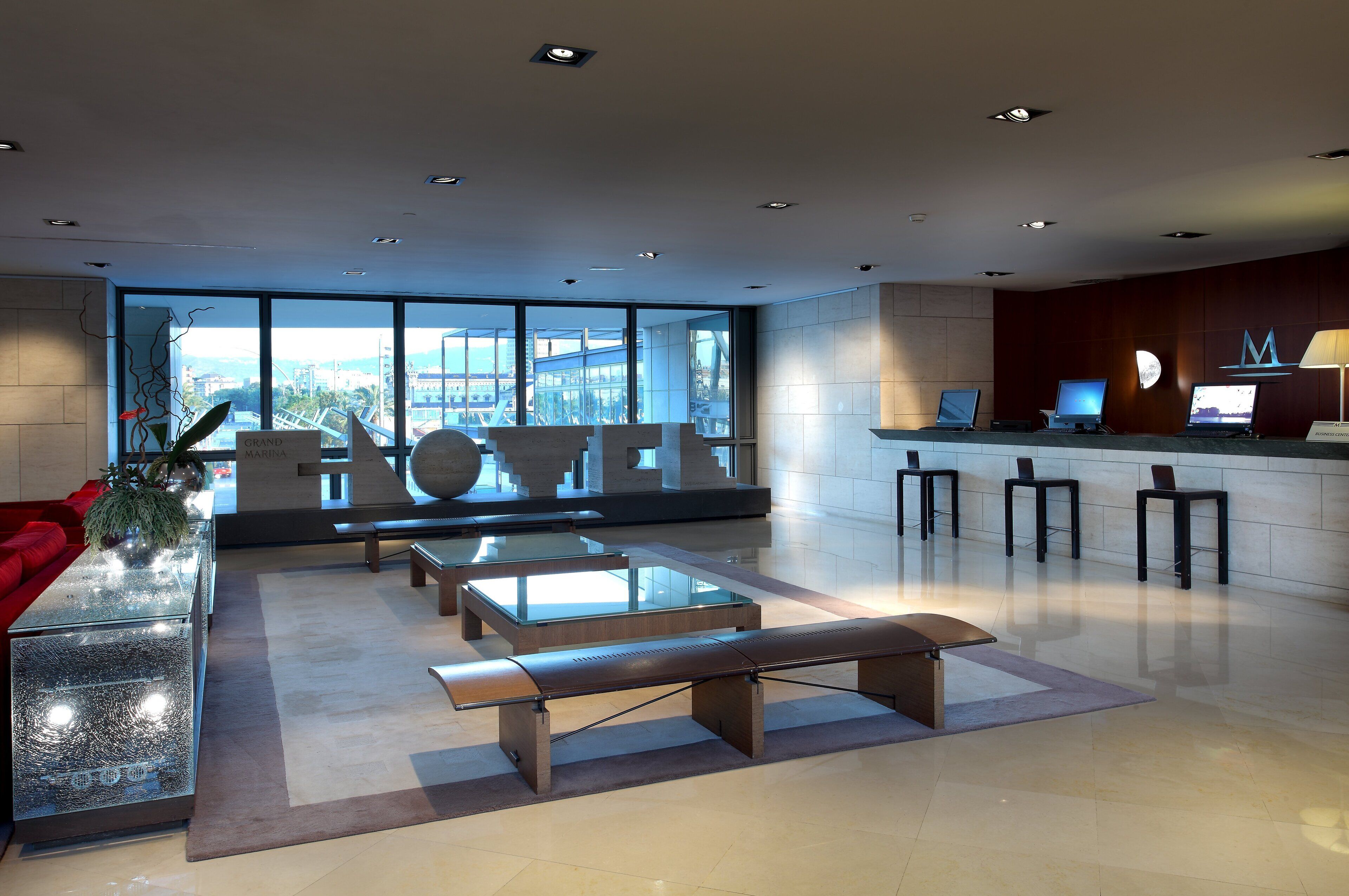 A modern lobby with a glass coffee table, benches, and a reception desk with computers.