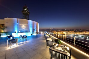 Um bar no terraço com assentos e vista para um rio ao entardecer.