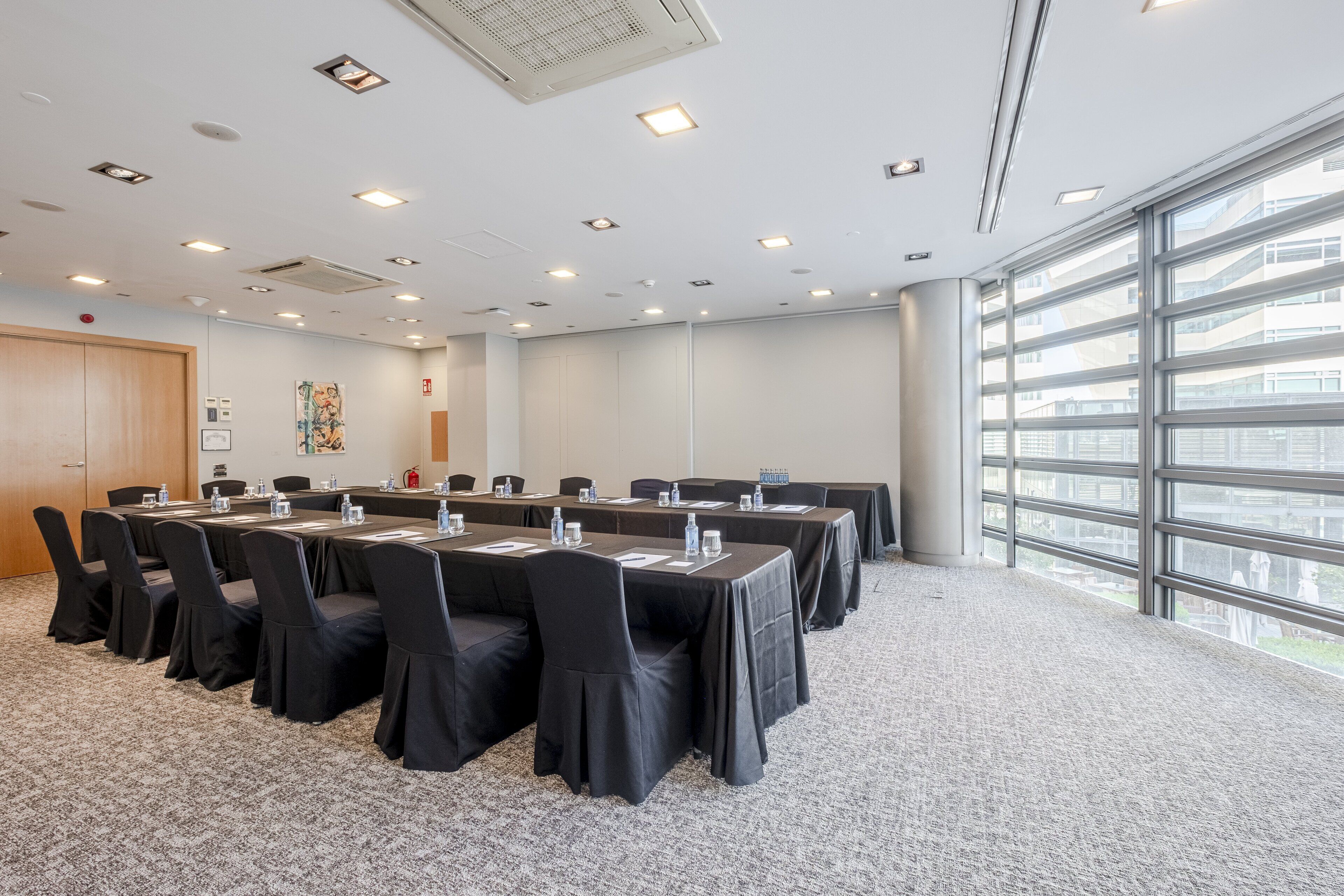 Une salle de conférence avec une longue table, des chaises noires et une grande fenêtre donnant sur la ville.