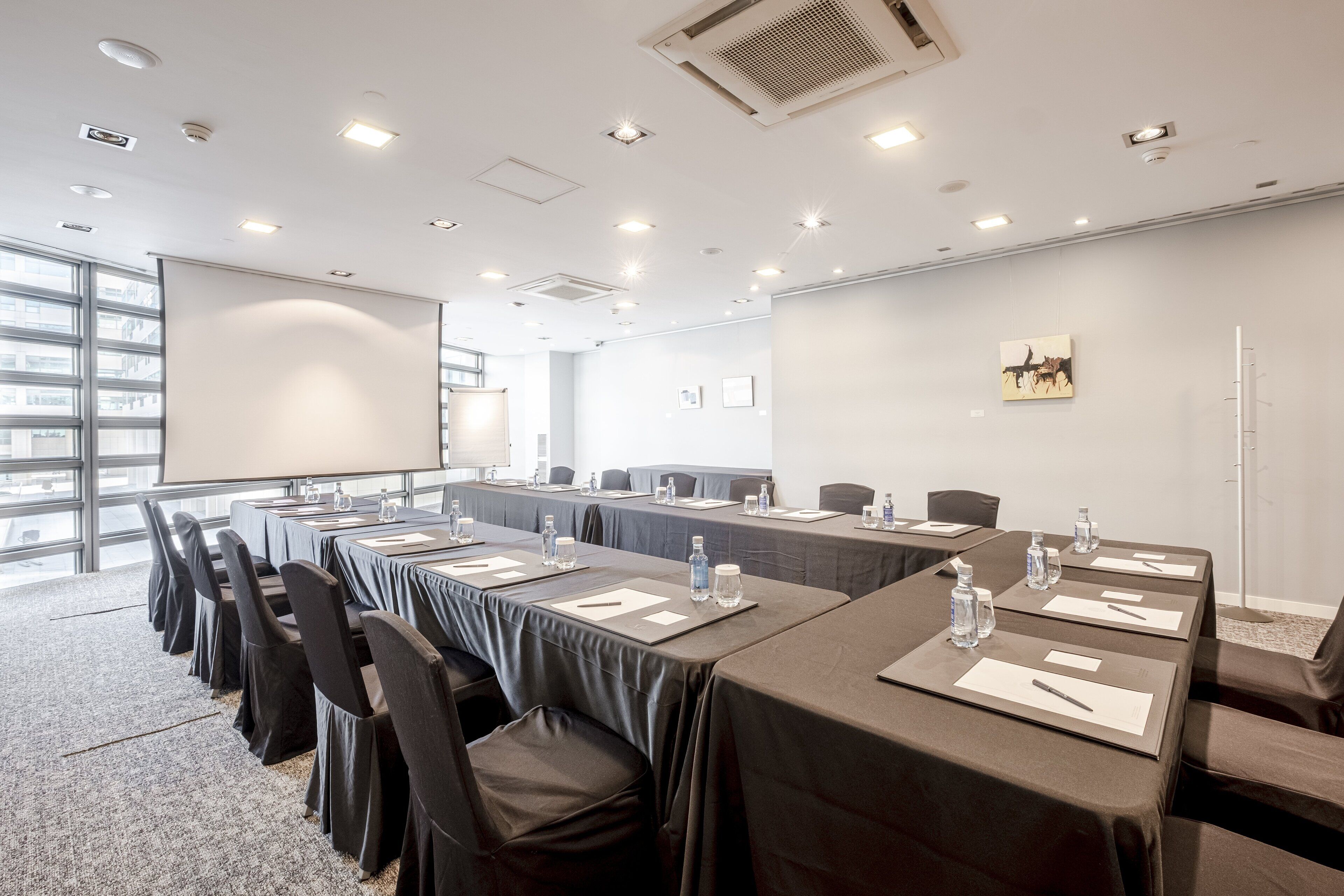 A conference room with long tables, chairs, and a projector screen.
