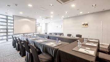 A conference room with long tables, chairs, and a projector screen.