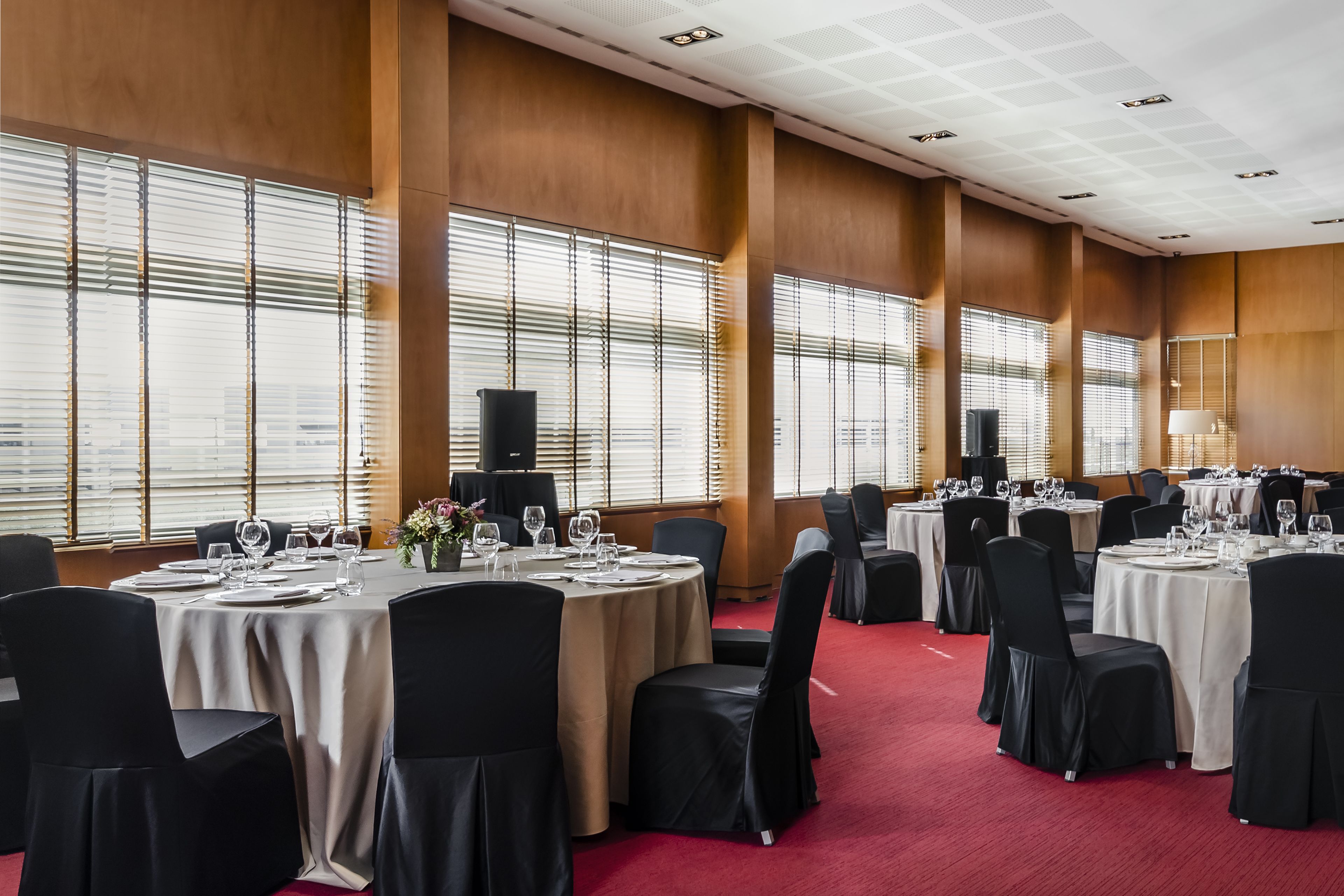 A conference room with multiple round tables, black chairs, and beige tablecloths.