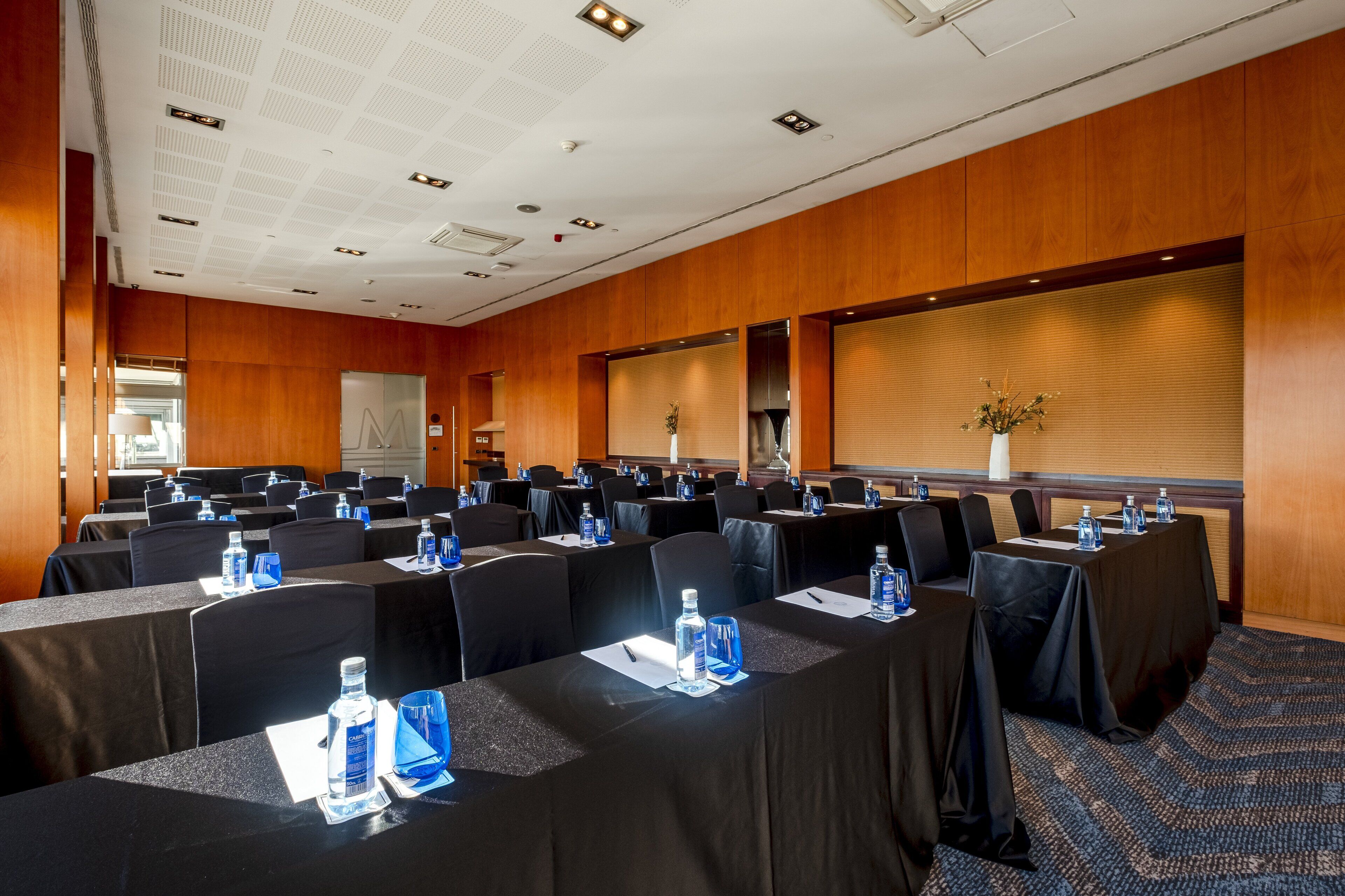 A conference room with rows of tables, black chairs, and water bottles.
