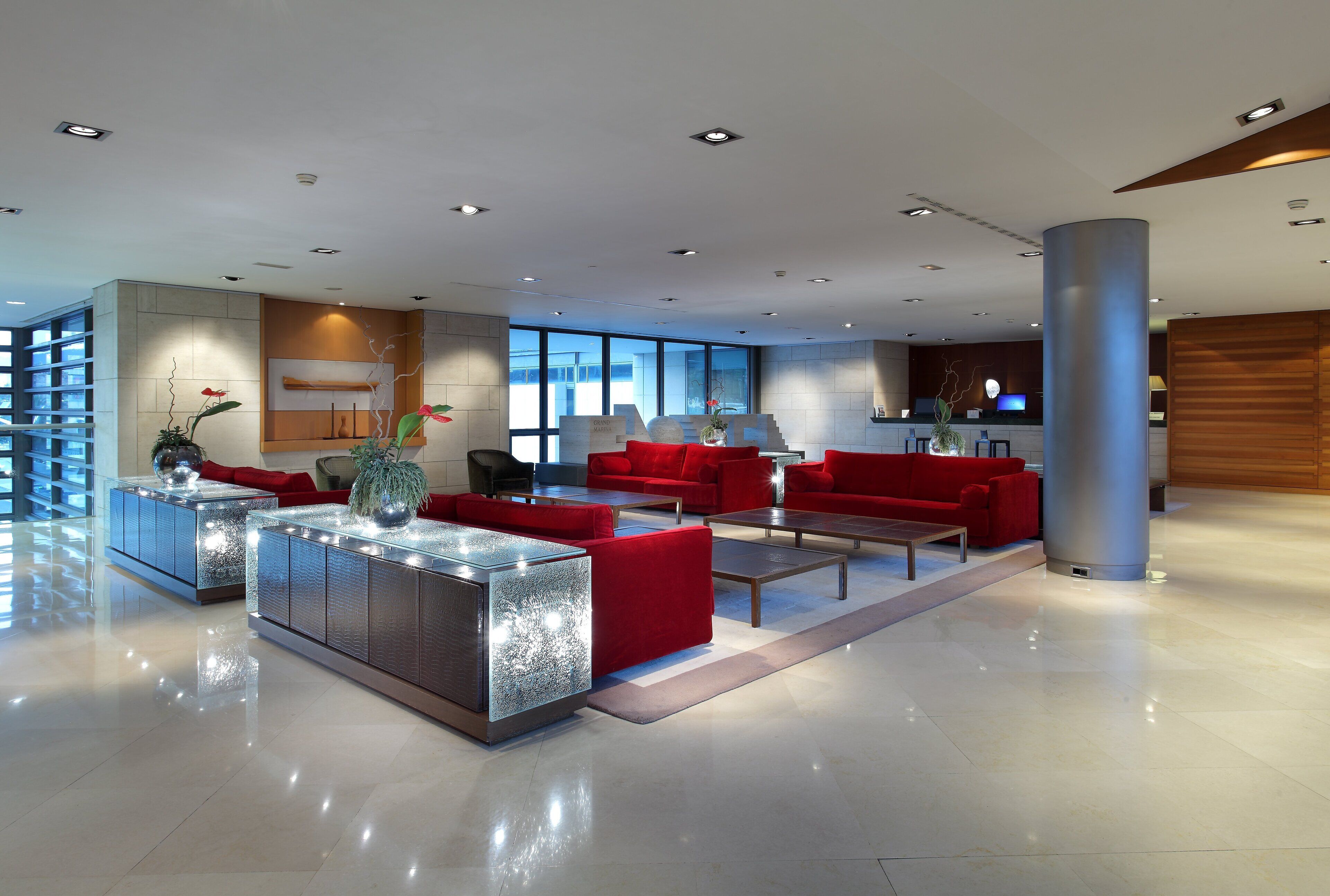 Un hall d’entrée moderne avec un comptoir d’accueil, des canapés rouges et une grande colonne.