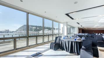 A conference room with large windows overlooking a harbor, equipped with tables and chairs.