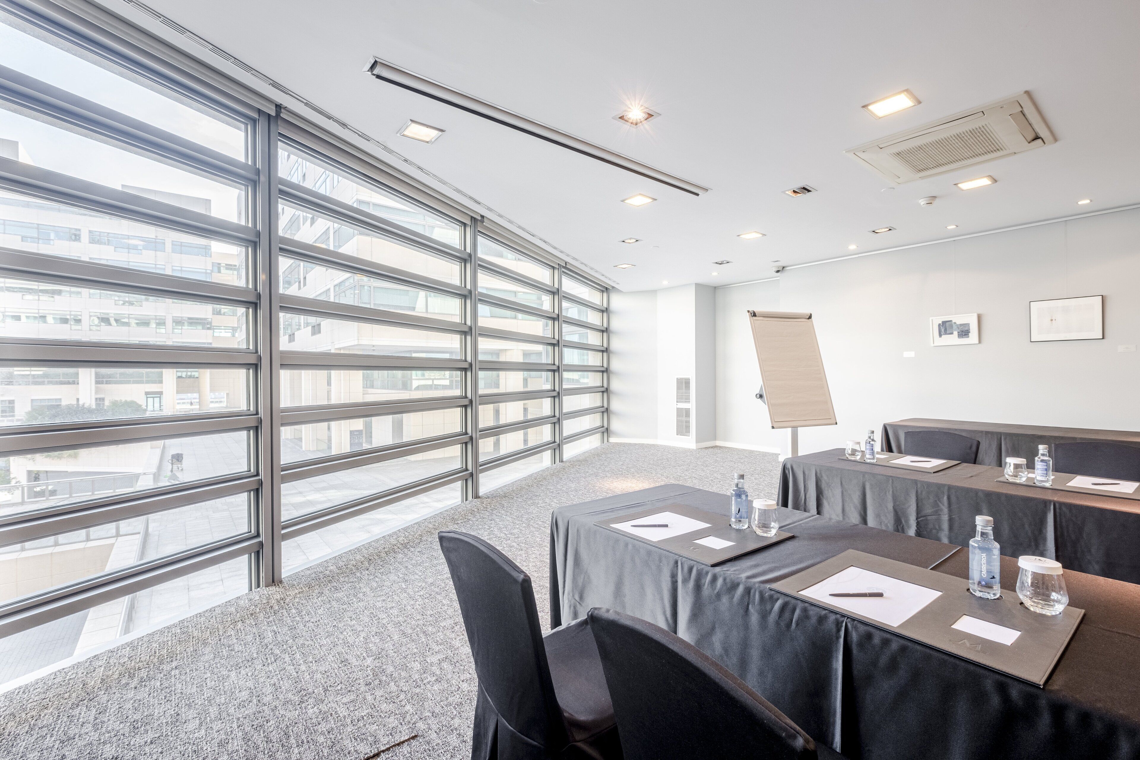 A conference room with large windows, tables with nameplates, water bottles, and a projector screen.